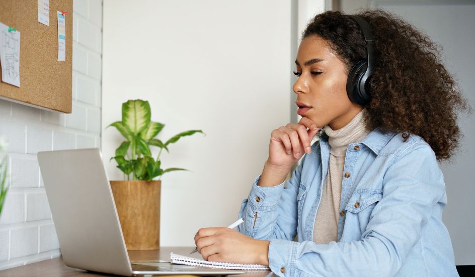 female sitting at desk looking at laptop wearing headphones
